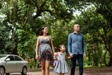 Fototapeta premium Pregnant mother, father, daughter walking in green park