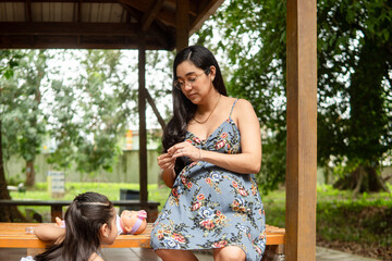 Pregnant mother and daughter playing with doll outdoors
