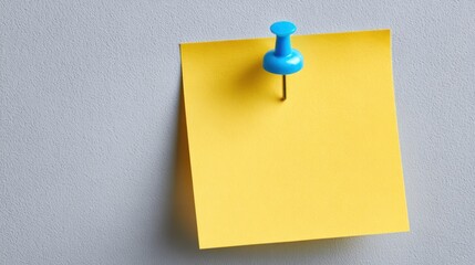 A bright yellow sticky note is fastened to a smooth gray wall with a blue pushpin. This setup highlights an organized space, ideal for reminders and messages in an office or home environment.