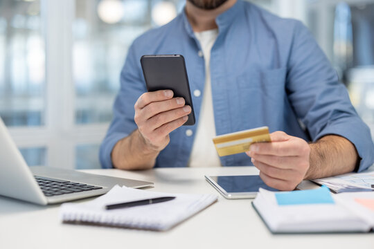 Man holding a smartphone and a credit card, engaging in online payment and e-commerce transactions from an office desk, showcasing modern digital finance and shopping