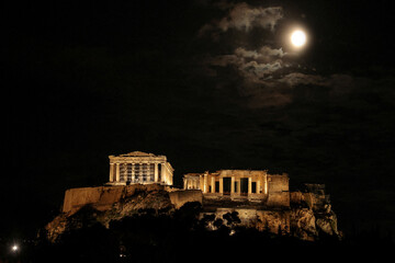 Ancient greek acropolis illuminated at night under a full moon and cloudy sky © Tayiba Studio