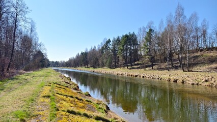 The river flows between grassy banks with a walking path. Birch, alder, spruce and pine trees grow...