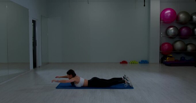 Athletic female resting prone position training floor spacious room sports equipment background