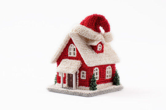 casita en miniatura hecha de ganchillo o crochet en tonos rojos y blancos con un gorro de pap&aacute; Noel en el tejado sobre fondo blanco con espacio vacio. Concepto celebraciones y compras navide&ntilde;as, 