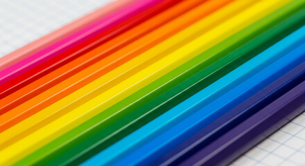 Closeup of a vibrant rainbow array of colored pencils lying diagonally across a white, subtly textured, gridlined surface