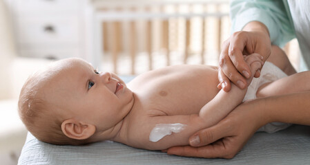 Mother applying cream onto her baby's arm on changing table at home, closeup