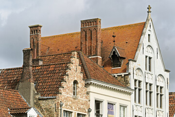 Obraz premium Group of historic buildings in Bruges, Belgium, showcasing steep red-tiled roofs, decorative brick chimneys, and gabled facades.