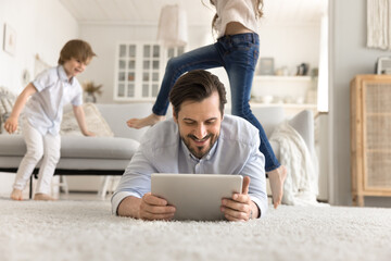 Smiling father relax using digital pad as kids jump around