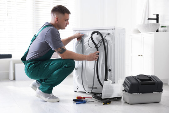 Fototapeta Repairman in uniform fixing broken washing machine at home