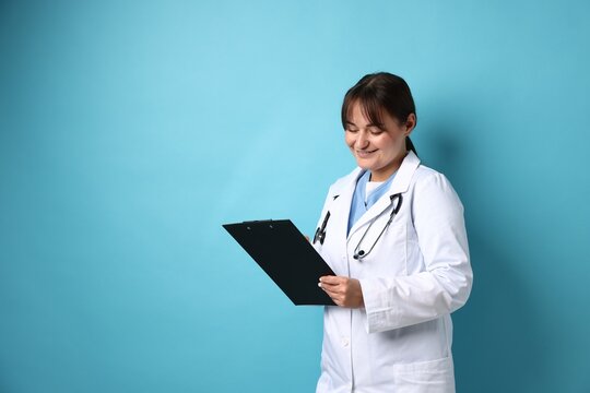 Doctor in medical uniform with stethoscope and clipboard on light blue background, space for text - Powered by Adobe
