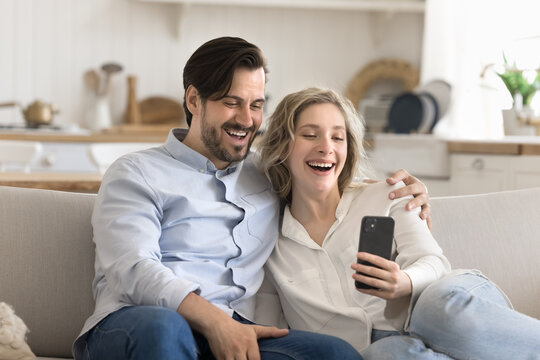 Overjoyed couple cuddle on couch laughing looking at phone screen