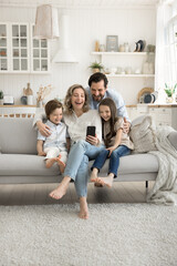 Happy mom dad two kids cuddle on couch using phone