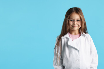 Cute little girl in laboratory coat and glasses on light blue background, space for text. Child and...