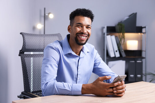 African-american man using smartphone at wooden table indoors - Powered by Adobe