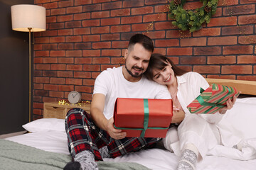Happy couple in pajamas with gift boxes spending time together on bed in room decorated for...