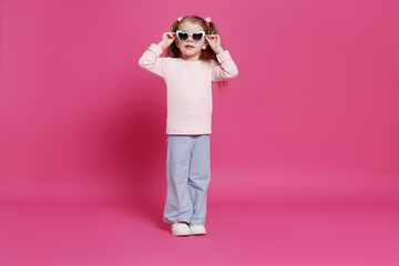 Cute little girl in sunglasses on pink background