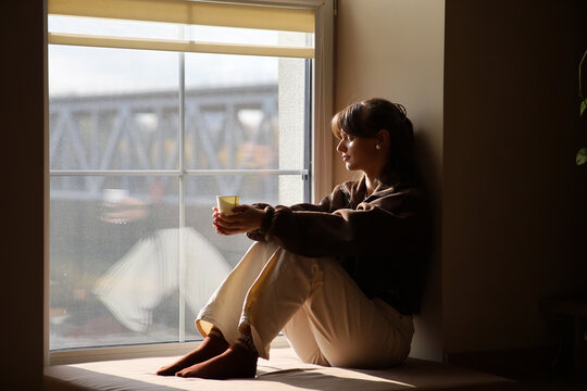 Pensive woman enjoying a quiet moment by the window with a warm drink
