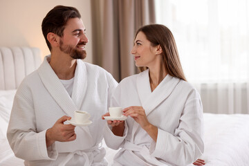 Happy couple in bathrobes with morning coffee on bed indoors