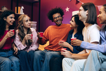 Diverse group of multinational young adults laughing and socializing at party in modern living room