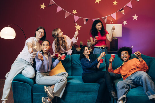Diverse group of multinational friends enjoying party with sparklers on sofa