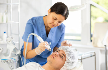 Fototapeta premium Female cosmetic doctor expertly administers procedure to male patient using hydrogen oxygen hydrating attachment.