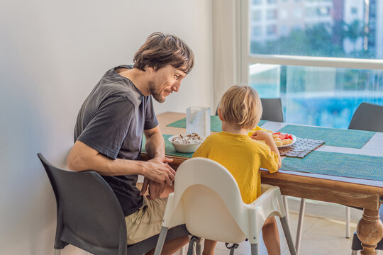 A father having breakfast at the table with his young son in a bright home kitchen, sharing a warm morning moment. Family bonding, parenting, everyday routine and healthy lifestyle concept