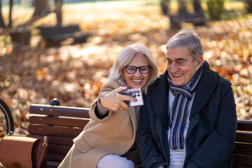 Happy senior couple taking a selfie in a park during autumn