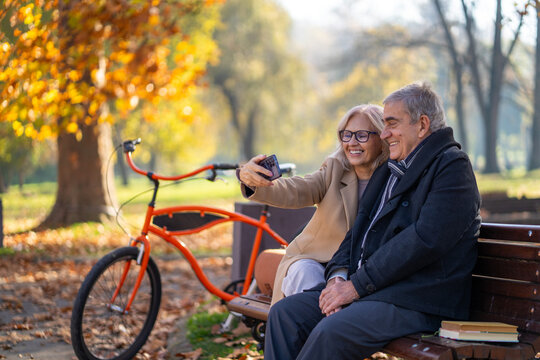 Happy senior couple taking a selfie in a park on a beautiful autumn day - Powered by Adobe