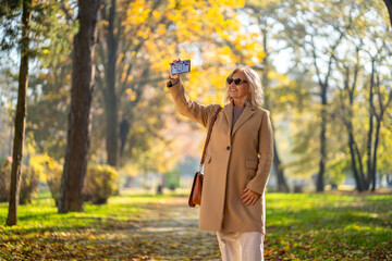 woman taking a selfie in a park during autumn with a smartphone