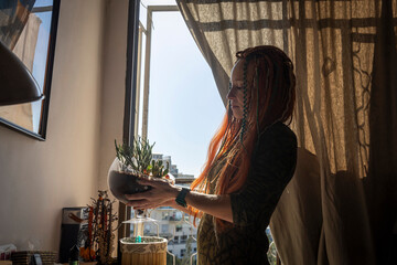 The silhouette of a calm woman with dreadlocks, standing thoughtfully by a sunlit window, holding a clear glass terrarium with succulents