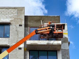 Worker using an articulated boom lift beside a building exterior under construction