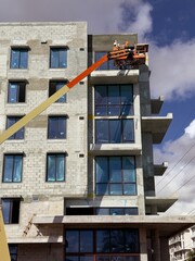 Worker using an articulated boom lift beside a building exterior under construction