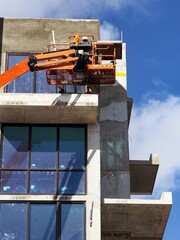 Worker using an articulated boom lift beside a building exterior under construction