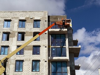Worker using an articulated boom lift beside a building exterior under construction