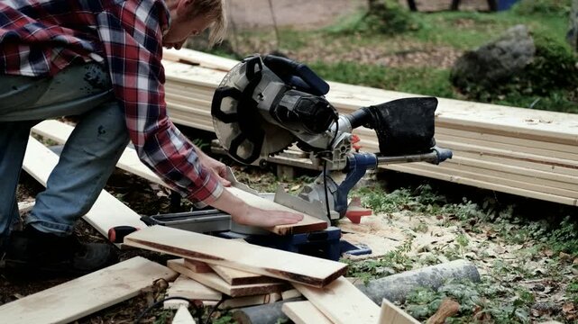 Woodworker operates a miter saw, cutting lumber in a natural outdoor setting