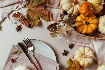 Ceramic plate with fork, knife, napkin and mini pumpkin on fall table with warm rustic decor..
