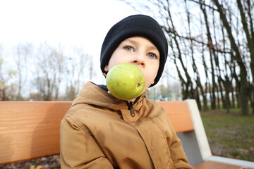 Child sitting on a park bench and eating a fresh pear during an autumn walk. Simple, natural moment highlighting healthy habits, outdoor lifestyle, and mindful childhood nutrition