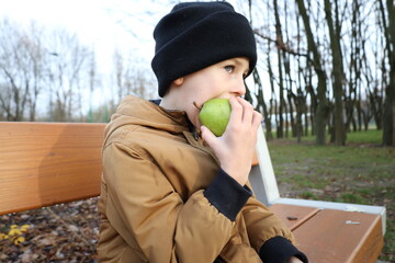Child sitting on a park bench and eating a fresh pear during an autumn walk. Simple, natural moment highlighting healthy habits, outdoor lifestyle, and mindful childhood nutrition