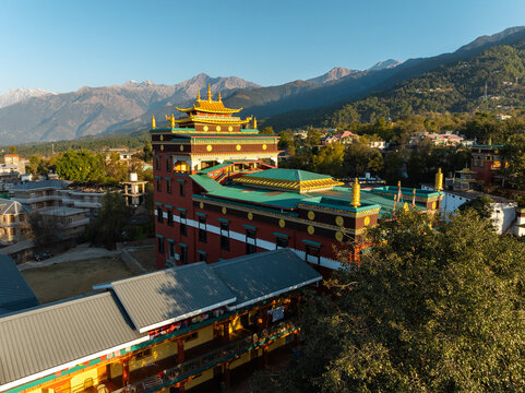 Aerial view of a Buddhist monastery with intricate architecture rising against a backdrop of majestic mountains, bathed in the warm glow of the sun, Bir, Himachal Pradesh, India.