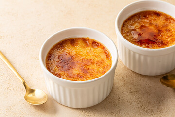 Creme brulee, or burnt cream,  a dessert consisting of a rich custard base topped with a layer of hardened caramelized sugar. Beige table surface.