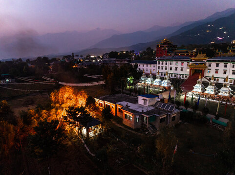 Aerial view of the serene monastery with illuminated stupas and vibrant prayer flags against the backdrop of the majestic Himalayas, Bir, Himachal Pradesh, India.