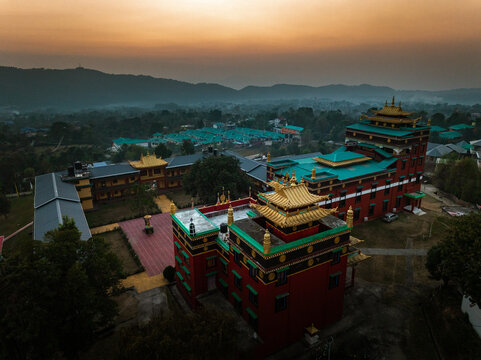 Aerial view of a monastery with vibrant red walls and golden roofs stands proudly against the backdrop of the serene, misty mountains, Bir, Himachal Pradesh, India.