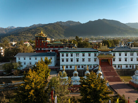 Aerial view of the serene golden-topped monastery complex contrasting against the backdrop of majestic mountains and clear skies, Bir, Himachal Pradesh, India.