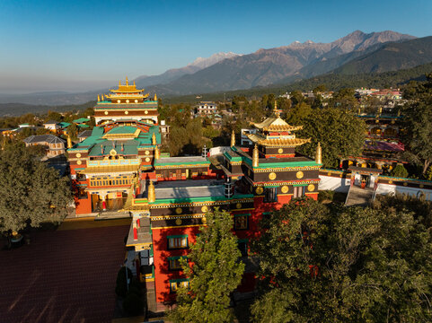 Aerial view of golden roofs glinting atop the Sherab Ling Monastery, a vibrant tapestry against the backdrop of the Dhauladhar range, Bir, Himachal Pradesh, India.