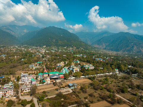 Aerial view of a valley nestled against the backdrop of majestic mountains, a tapestry of earthy tones contrasting with the vibrant greens of the vegetation, Bir, Himachal Pradesh, India.