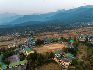Aerial view of buildings nestled amidst rolling hills and lush greenery, a tranquil scene blending architecture with nature's grandeur, Baijnath, Himachal Pradesh, India.