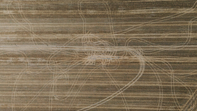 Abstract top-down aerial view of a harvested field showing complex patterns of tire tracks overlaid on the linear stubble