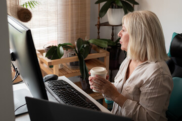 Senior woman working from home using computer drinking coffee