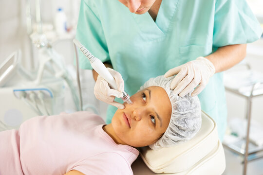 Young cosmetic doctor confidently utilizes hydrogen oxygen cleaning attachment on machine, providing client with impeccable skincare.