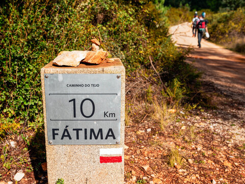 Trail marker showing 10 km to F&aacute;tima on Caminho do Tejo pilgrimage route, Portugal. Distance sign with pilgrims walking on scenic path with stacked stones